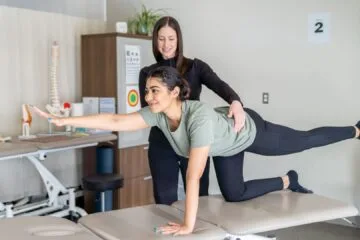 A woman performs a stretching exercise with the guidance of a pelvic floor physical therapist in a clinical setting.