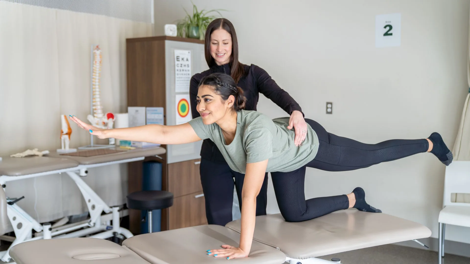A woman performs a stretching exercise with the guidance of a pelvic floor physical therapist in a clinical setting.