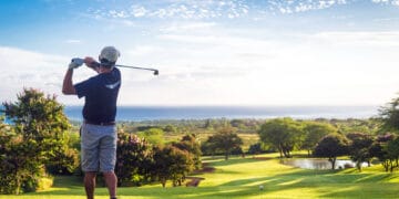 A man swings a golf club on a lush green field, focusing intently on his shot.