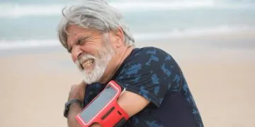 Man gripping his shoulder in pain at the beach.