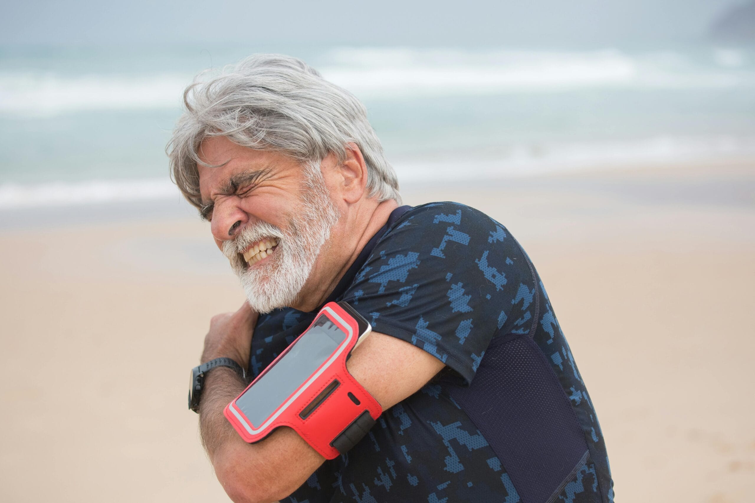 Man gripping his shoulder in pain at the beach.