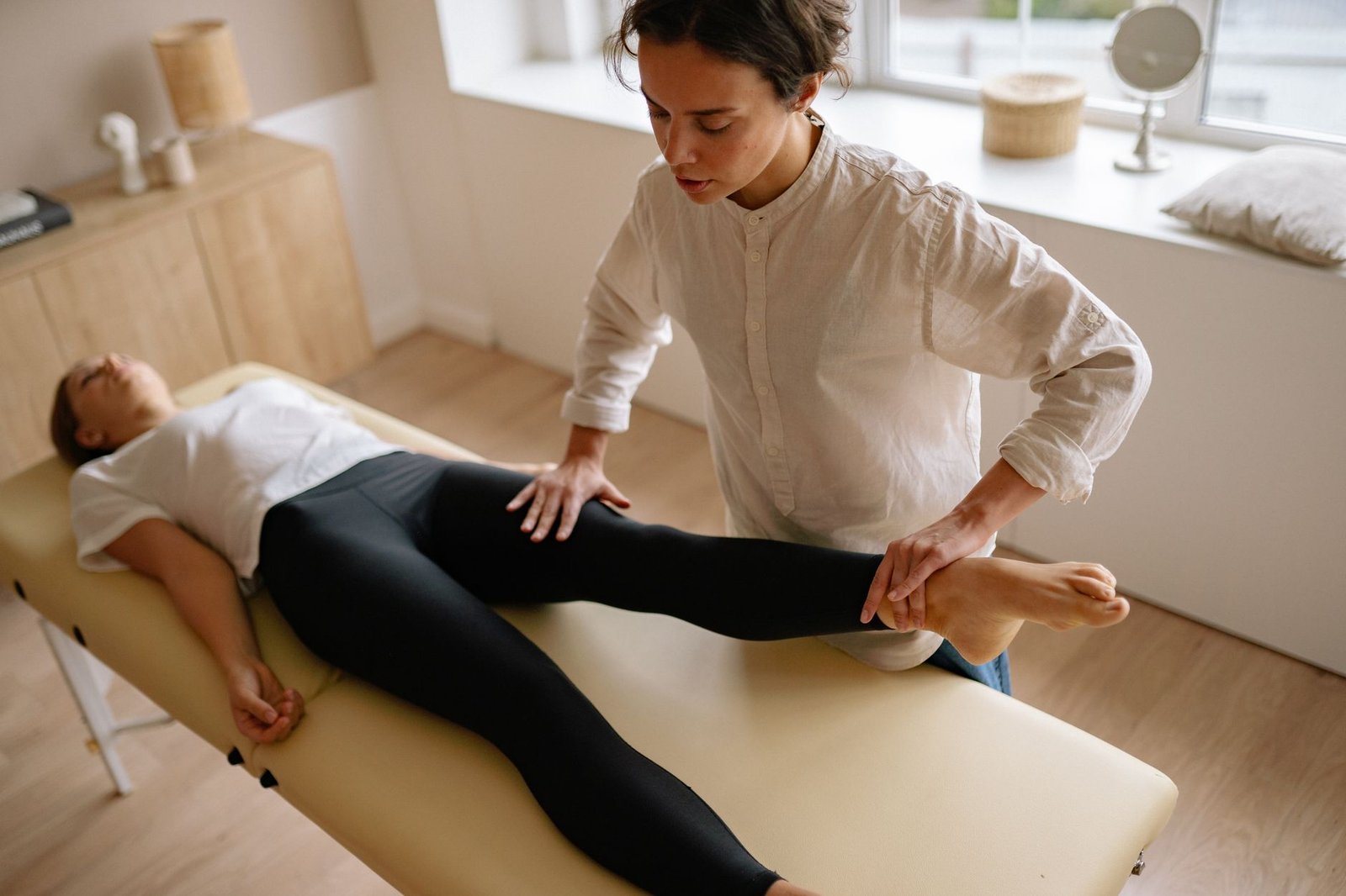 A physiotherapist assists a woman with leg rehabilitation therapy in a calm treatment room