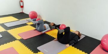 Women in a yoga class using exercise balls on colorful mats indoors.