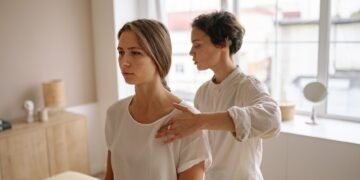 A woman receives shoulder therapy from a therapist in a serene room with natural light.
